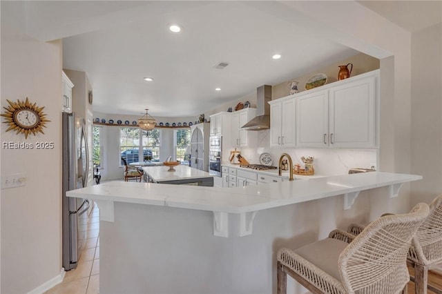 kitchen featuring appliances with stainless steel finishes, a breakfast bar area, white cabinets, kitchen peninsula, and wall chimney exhaust hood