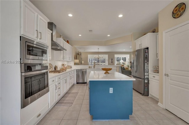 kitchen featuring white cabinetry, stainless steel appliances, a center island, kitchen peninsula, and wall chimney exhaust hood