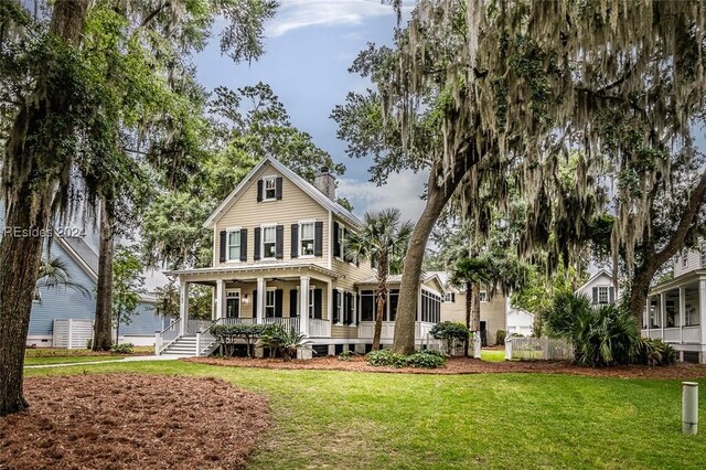 back of property with a sunroom, covered porch, and a lawn