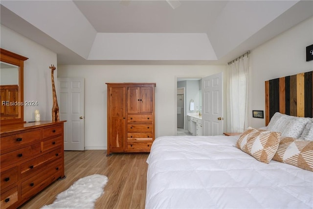 bedroom with ensuite bath, a tray ceiling, and light hardwood / wood-style flooring