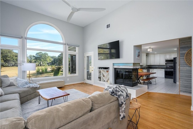 living room with ceiling fan, light hardwood / wood-style floors, and a high ceiling