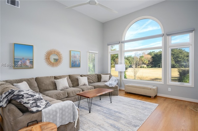 living room featuring ceiling fan, light hardwood / wood-style floors, and a towering ceiling