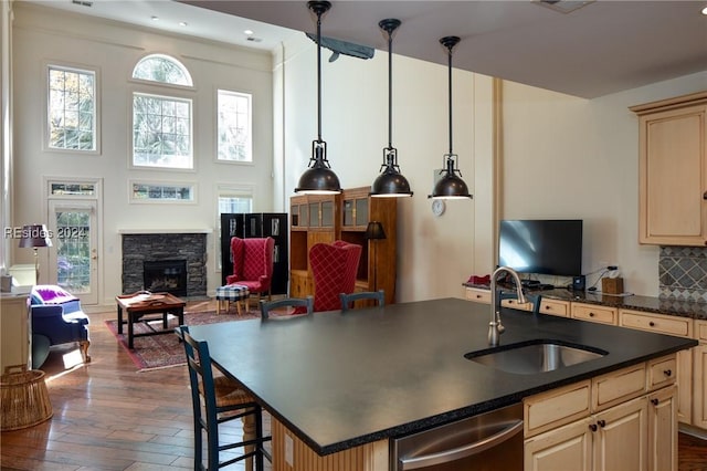 kitchen with sink, dishwasher, hanging light fixtures, backsplash, and an island with sink