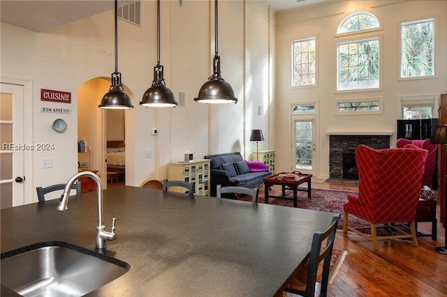 kitchen featuring a stone fireplace, pendant lighting, sink, a high ceiling, and dark wood-type flooring