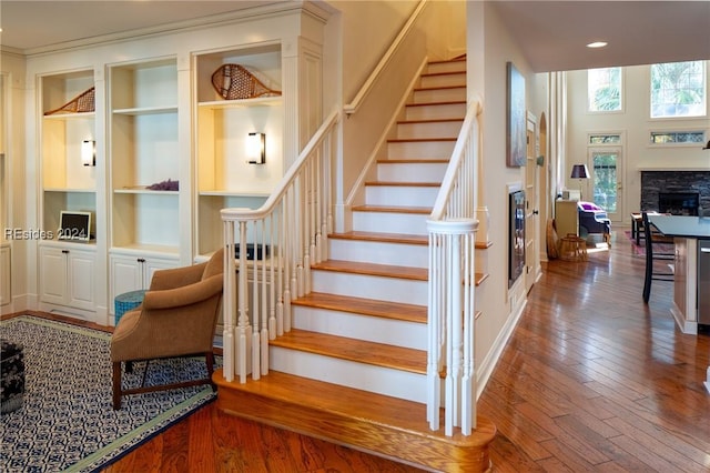 stairs featuring built in shelves, a stone fireplace, and hardwood / wood-style floors