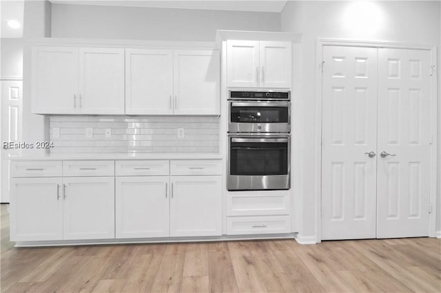 kitchen featuring light wood-type flooring, double oven, tasteful backsplash, and white cabinets