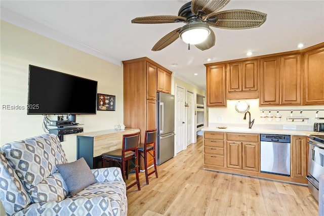 kitchen with sink, crown molding, light wood-type flooring, appliances with stainless steel finishes, and ceiling fan