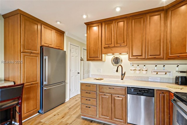 kitchen featuring sink, ornamental molding, light hardwood / wood-style floors, and appliances with stainless steel finishes