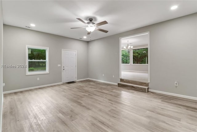 spare room featuring ceiling fan with notable chandelier and light wood-type flooring