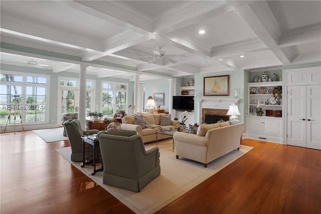 living room with beam ceiling, a brick fireplace, built in shelves, and ornate columns