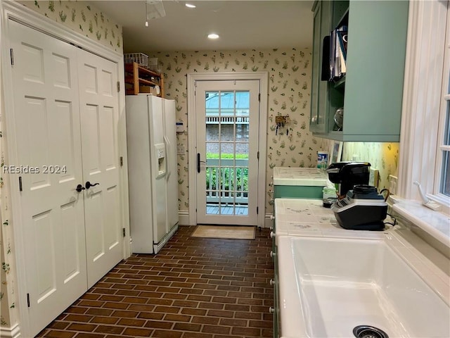 interior space with sink, white fridge with ice dispenser, and green cabinets