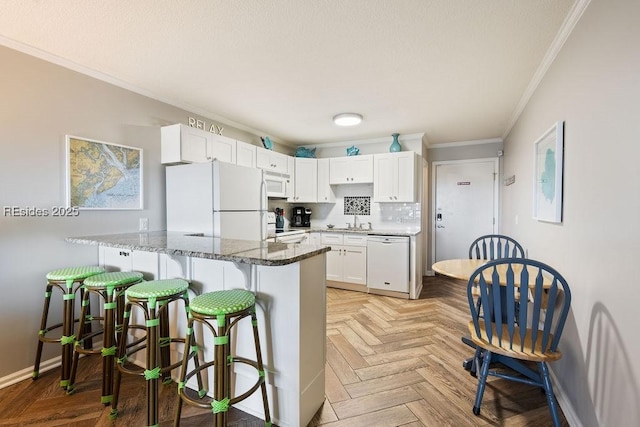 kitchen featuring a kitchen bar, white cabinetry, crown molding, white appliances, and dark stone counters