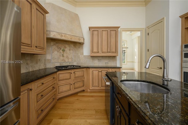 kitchen with premium range hood, appliances with stainless steel finishes, sink, dark stone counters, and light wood-type flooring