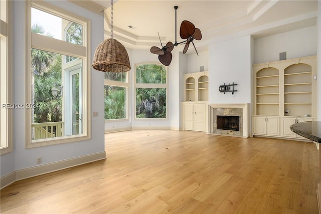 unfurnished living room featuring built in shelves, plenty of natural light, a fireplace, and light hardwood / wood-style flooring