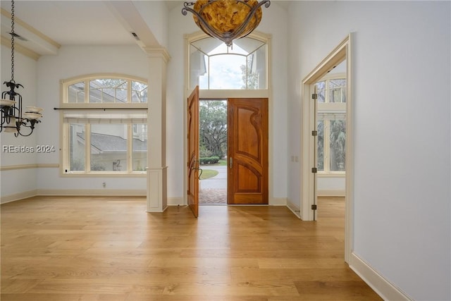 foyer entrance featuring decorative columns, a notable chandelier, and light wood-type flooring