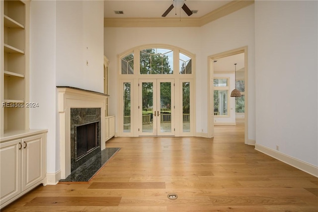 unfurnished living room with a high end fireplace, ceiling fan, crown molding, light wood-type flooring, and french doors