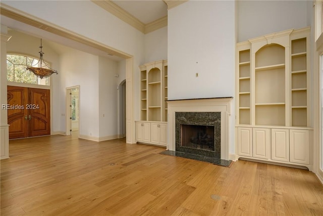 unfurnished living room featuring built in shelves, crown molding, a towering ceiling, a high end fireplace, and light hardwood / wood-style floors