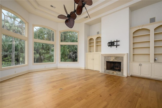 unfurnished living room with built in features, ceiling fan, a high end fireplace, light hardwood / wood-style floors, and a high ceiling