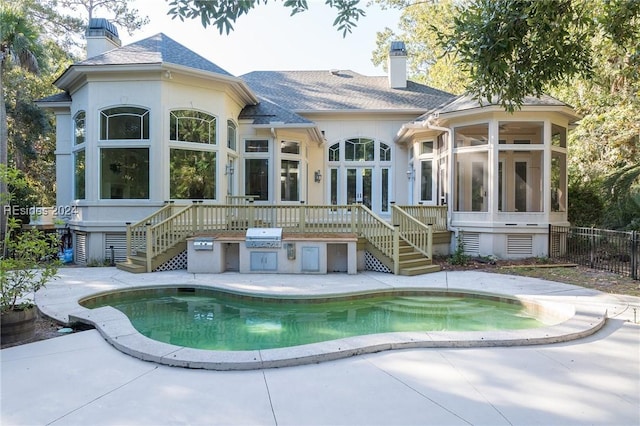 rear view of house with a fenced in pool, a sunroom, an outdoor kitchen, and a patio area