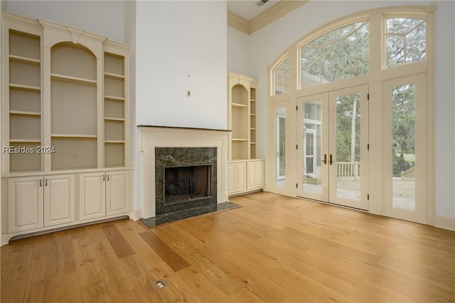 unfurnished living room featuring light hardwood / wood-style flooring, built in features, a premium fireplace, a high ceiling, and ornamental molding