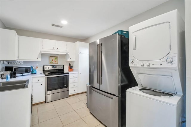 kitchen with sink, light tile patterned floors, appliances with stainless steel finishes, stacked washing maching and dryer, and white cabinets