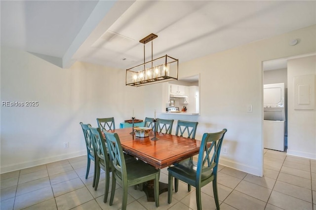 tiled dining area with stacked washer / drying machine and a chandelier