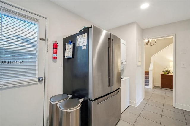 kitchen featuring stacked washer / dryer, white cabinetry, light tile patterned floors, and stainless steel fridge