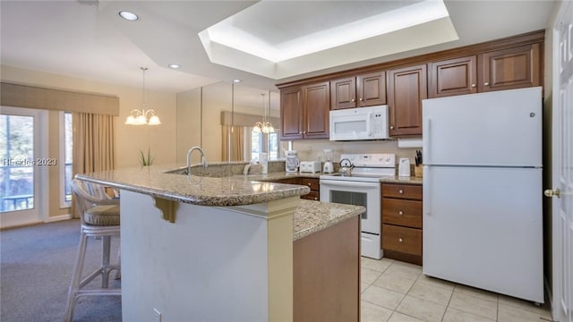 kitchen with pendant lighting, white appliances, a tray ceiling, and a kitchen breakfast bar