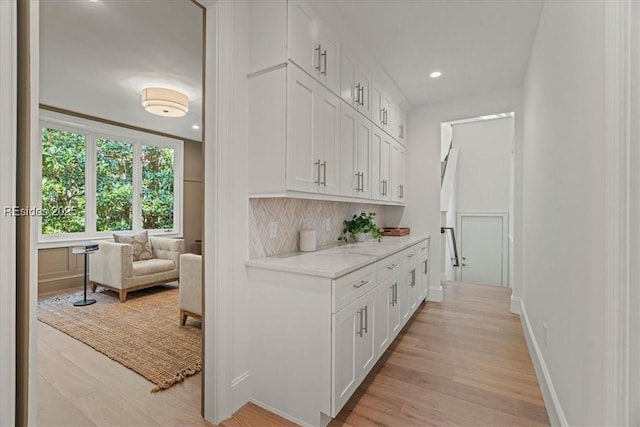 bar featuring backsplash, light hardwood / wood-style flooring, light stone countertops, and white cabinets