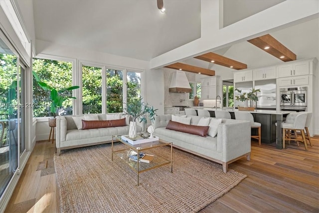 living room featuring sink, plenty of natural light, beam ceiling, and light hardwood / wood-style floors