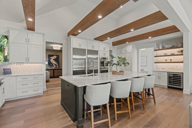 kitchen with tasteful backsplash, white cabinetry, sink, beverage cooler, and a spacious island