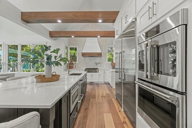 kitchen featuring a large island with sink, custom exhaust hood, stainless steel appliances, and white cabinets