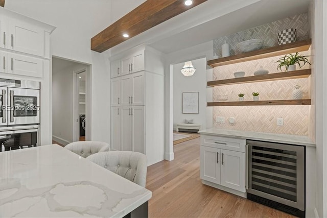 kitchen with white cabinetry, light hardwood / wood-style flooring, double oven, beverage cooler, and light stone countertops