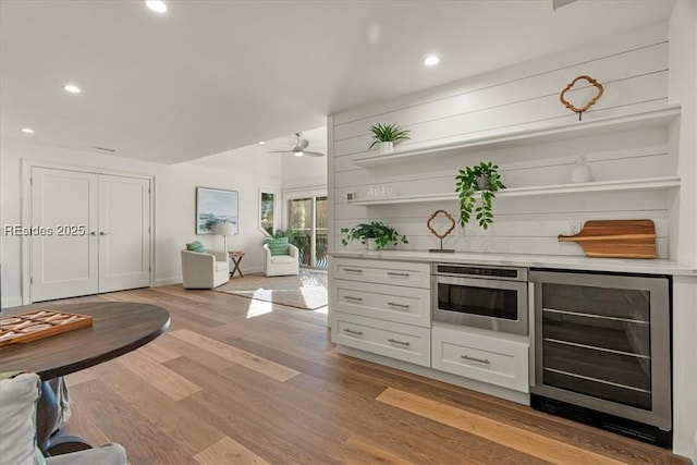 bar with wine cooler, ceiling fan, light hardwood / wood-style flooring, and white cabinets