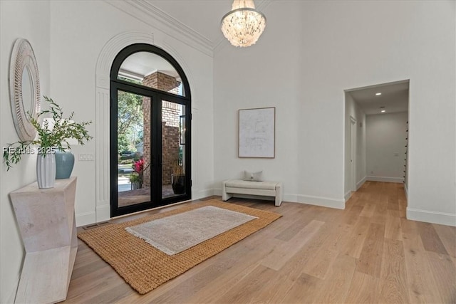 entrance foyer with crown molding, light hardwood / wood-style floors, an inviting chandelier, and french doors