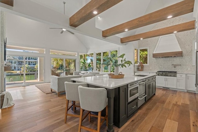 kitchen with sink, custom exhaust hood, a center island, beamed ceiling, and white cabinets