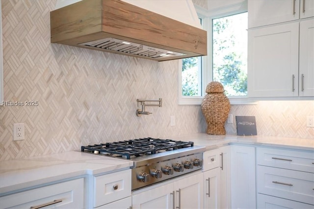 kitchen featuring stainless steel gas stovetop, custom range hood, white cabinets, and light stone counters