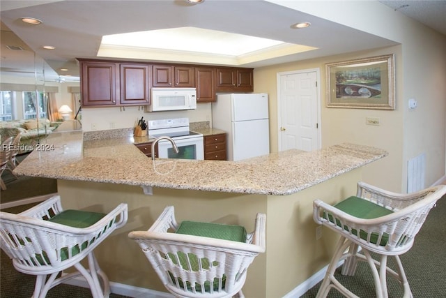 kitchen with a breakfast bar area, crown molding, kitchen peninsula, a raised ceiling, and white appliances