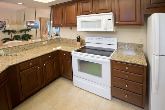 kitchen with light tile patterned floors, white appliances, light stone countertops, and kitchen peninsula