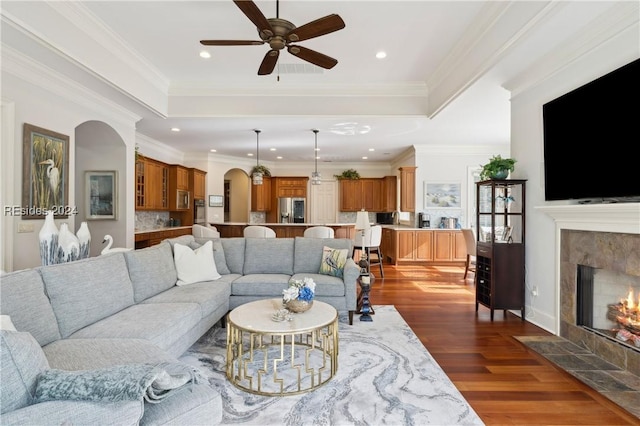 living room featuring crown molding, ceiling fan, dark hardwood / wood-style floors, and a tiled fireplace