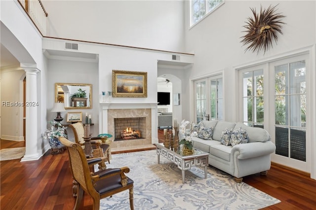 living room with ornate columns, hardwood / wood-style flooring, a towering ceiling, and a high end fireplace