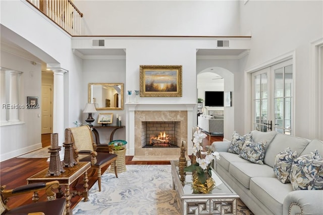 living room featuring french doors, hardwood / wood-style floors, a towering ceiling, a high end fireplace, and decorative columns