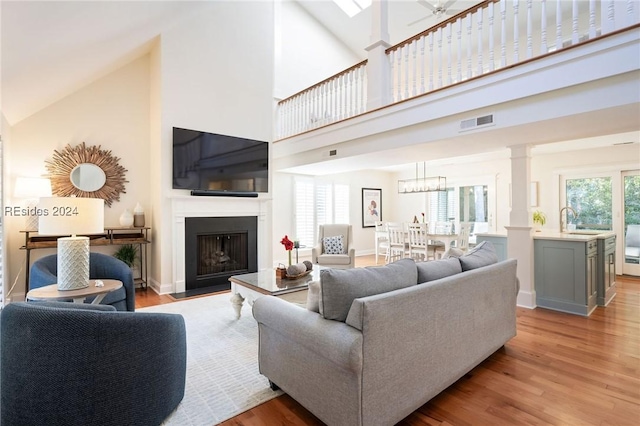 living room featuring high vaulted ceiling, decorative columns, sink, ceiling fan, and light hardwood / wood-style floors