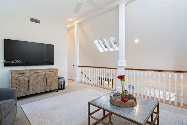 carpeted living room with ornate columns, lofted ceiling with skylight, and ceiling fan