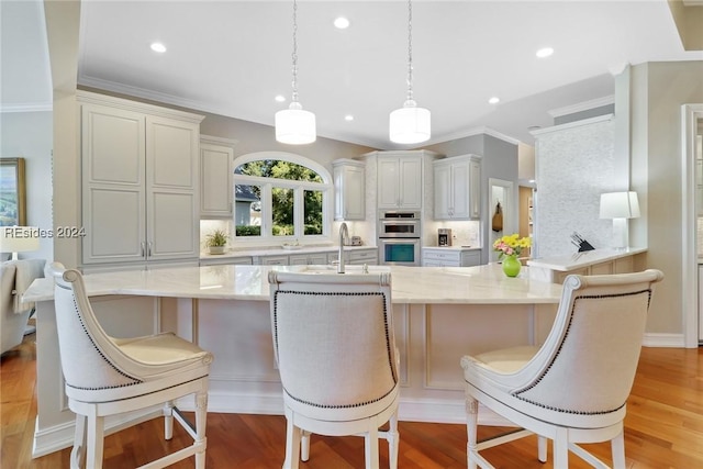 kitchen with double oven, decorative light fixtures, a kitchen breakfast bar, decorative backsplash, and light wood-type flooring