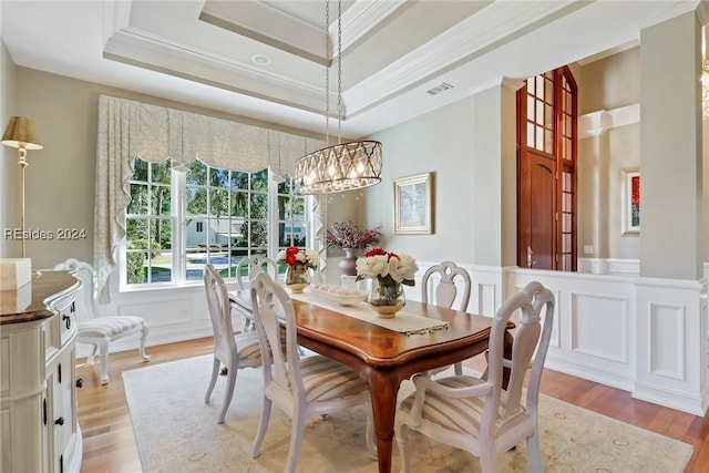 dining space featuring crown molding, a notable chandelier, a tray ceiling, and light hardwood / wood-style floors