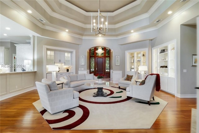 living room with a notable chandelier, a tray ceiling, light hardwood / wood-style floors, and built in shelves