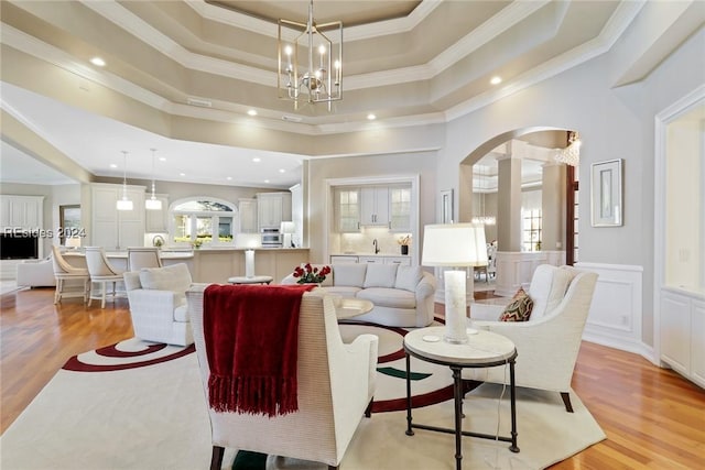 living room with a towering ceiling, a tray ceiling, crown molding, an inviting chandelier, and light hardwood / wood-style flooring