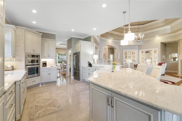 kitchen featuring light stone counters, pendant lighting, decorative backsplash, and a large island with sink