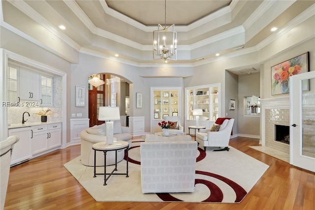 living room with a chandelier, light hardwood / wood-style flooring, a tray ceiling, a premium fireplace, and a high ceiling